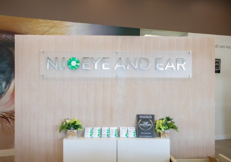 The image shows an interior space with a sign that reads NUJUYE AND EAR above a counter, indicating the name of a business. There are items on the counter including what appears to be a gift bag and possibly some pamphlets or brochures, suggesting this is a retail or promotional area. The setting has a modern aesthetic with a clean and minimalist design.