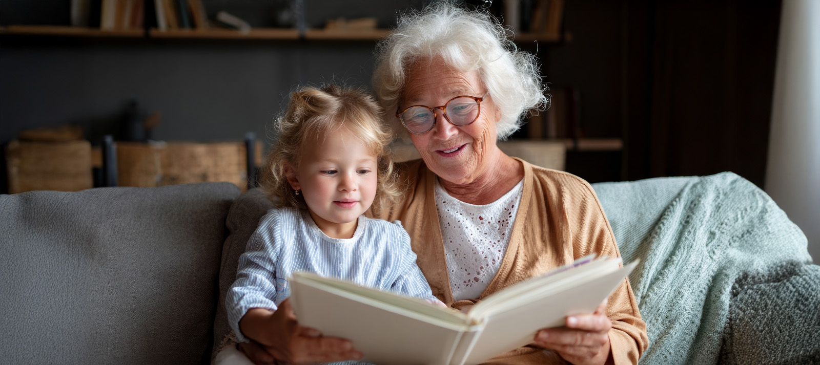 The image shows an older woman seated on a couch with a young child on her lap, both engaged in reading a book together.