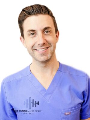 The image shows a man wearing a blue scrub top with a logo on the left chest area, smiling at the camera.
